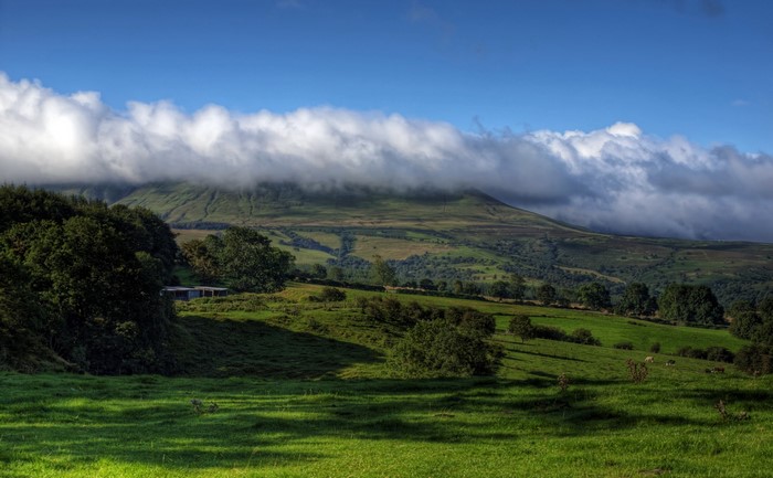 Rolling green hills with clouds over mountains in Wales