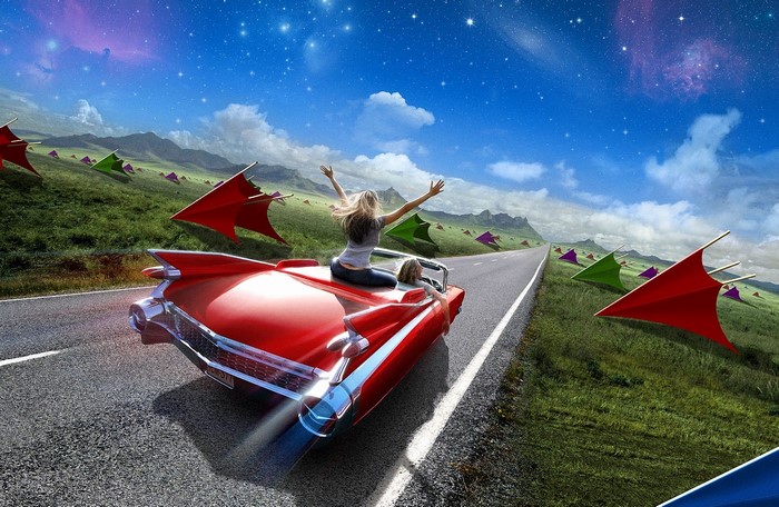 People in a red convertible driving on a road with kites