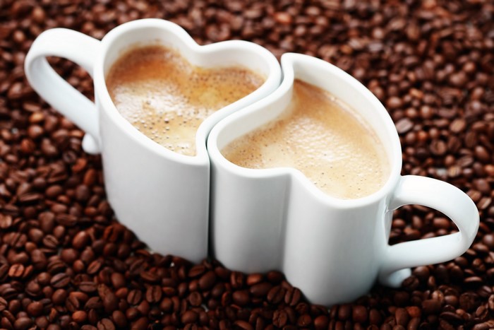 Two heart-shaped coffee mugs filled with coffee on coffee beans