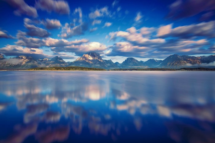 Grand Teton Mountains reflected in a calm lake under a cloudy sky