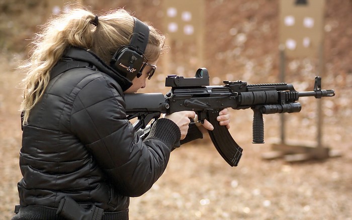 Woman with blonde ponytail shooting an assault rifle