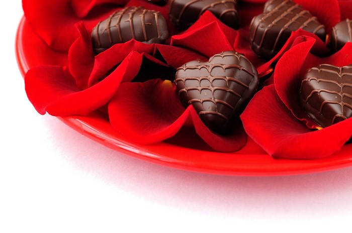 Heart-shaped chocolates on red rose petals on a red plate