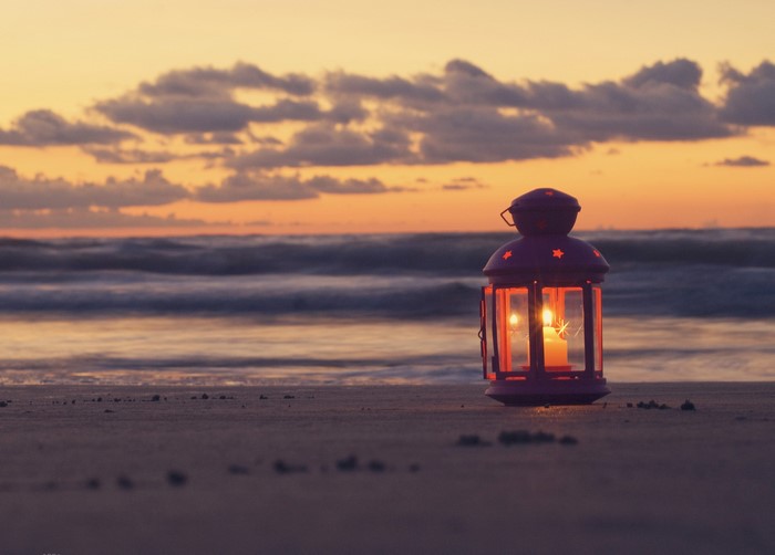 Lantern with candle on beach at sunset