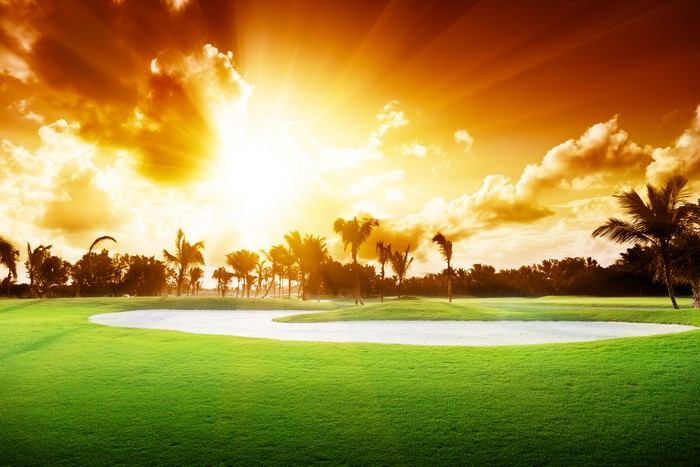 Golf course with sand trap and palm trees at sunset