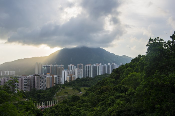 Apartment buildings nestled in a valley with a mountain backdrop under cloudy skies