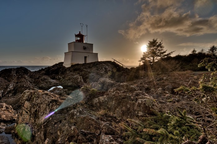 White lighthouse on rocky shore with sun rays
