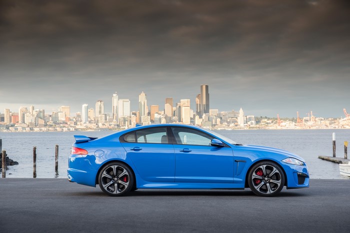 Blue Jaguar XFR-S parked by a city skyline