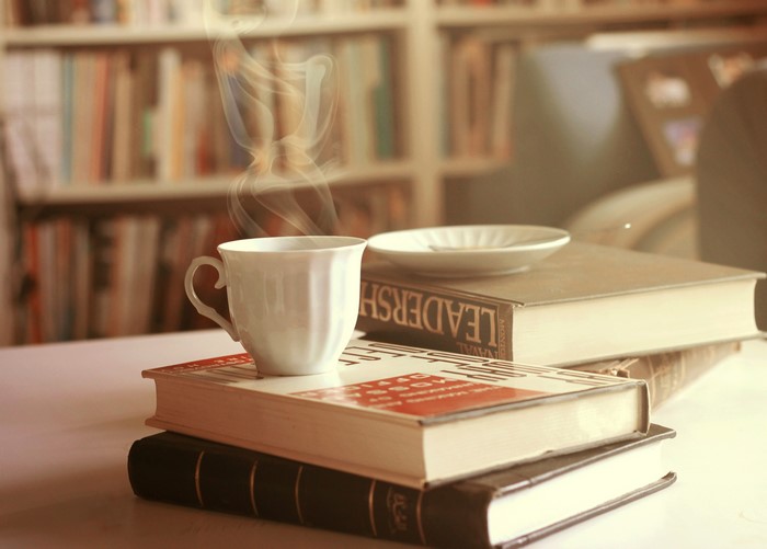 Cup of steaming coffee on books in library