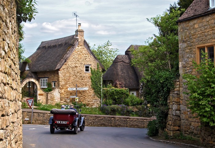 Vintage car driving through a Cotswolds village