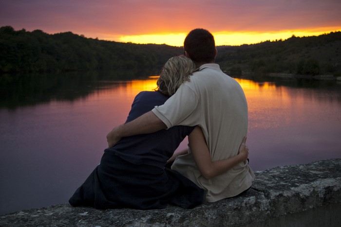 Couple hugging by the lake at sunset