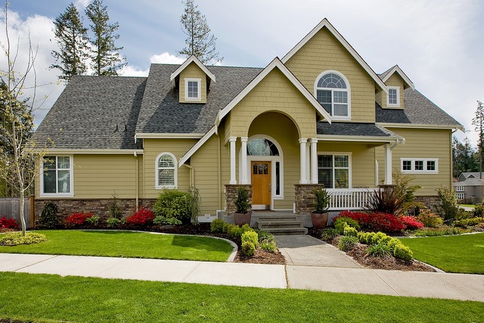 Yellow suburban house with arched entryway and manicured lawn