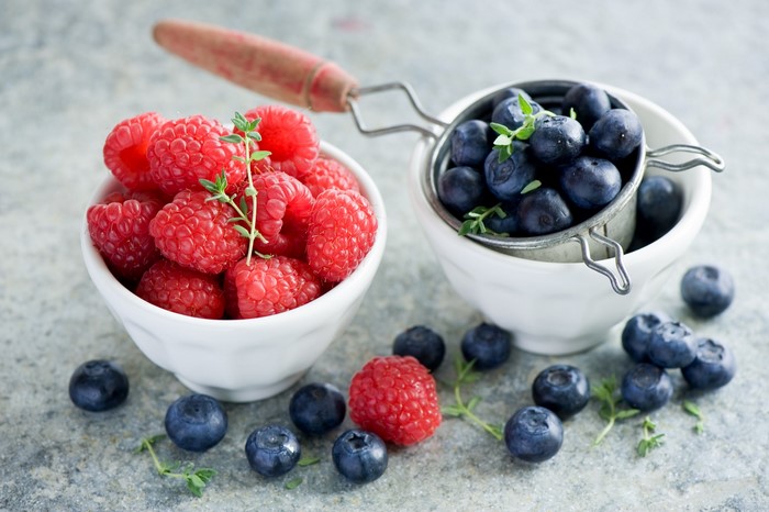 Raspberries and blueberries in bowls with thyme