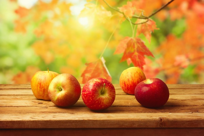 Apples on a wooden table with autumn foliage