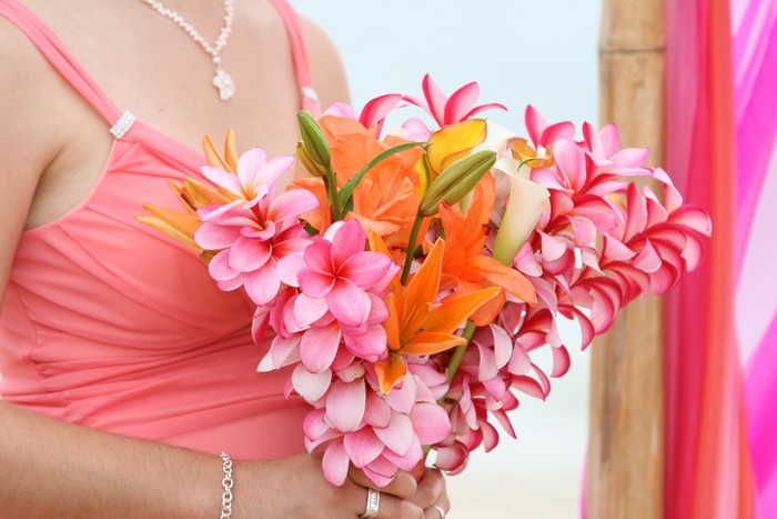 Woman in coral dress holding a bouquet of plumeria and lilies