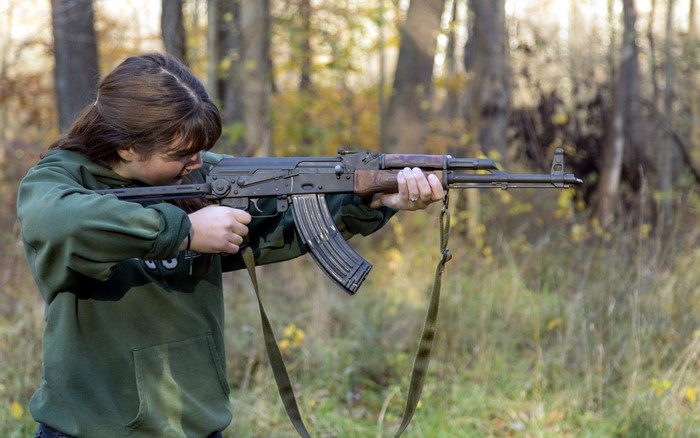 Girl holding an AK-47 rifle outdoors