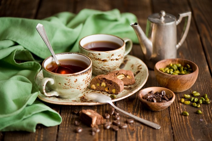 Two cups of tea with biscotti and pistachios