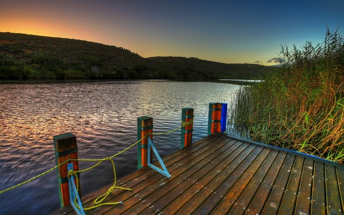 Wooden dock on a river at sunset with reeds