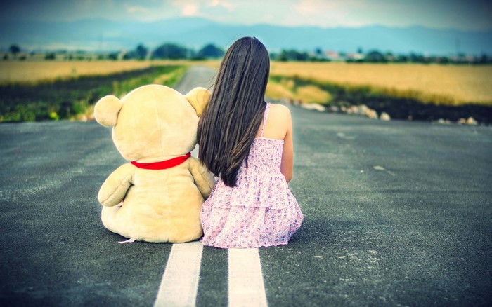 Girl and teddy bear sitting on a road