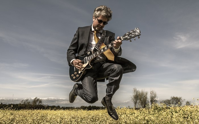 Man in Suit Jumping with Guitar in Field