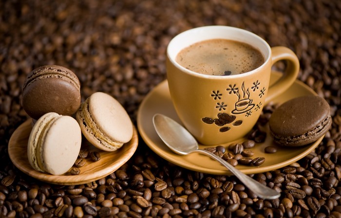 Coffee cup with macarons and spoon on coffee beans