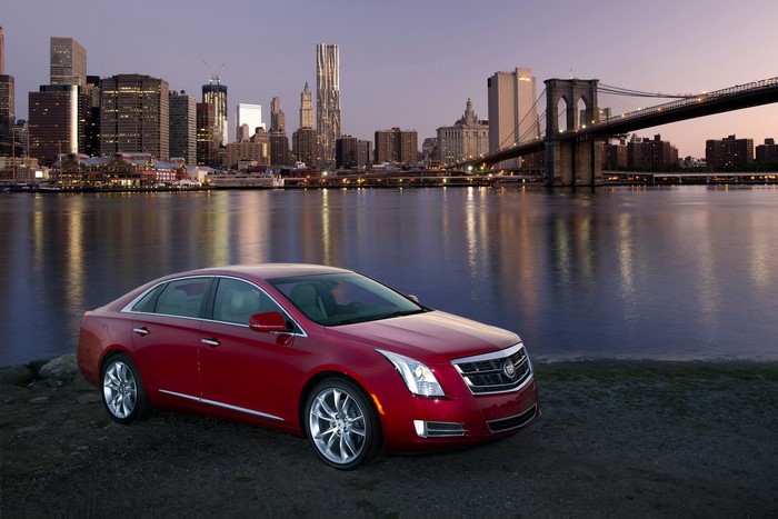 Red Cadillac XTS Vsport parked by Brooklyn Bridge and Manhattan skyline