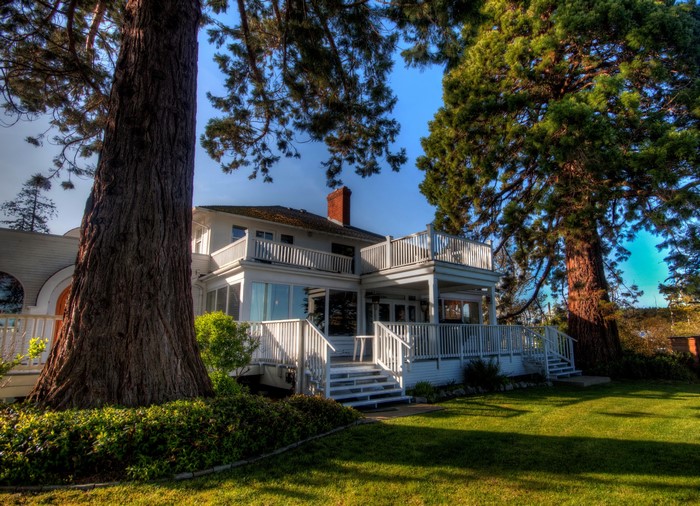 White house with decks and large trees in North Saanich, Canada