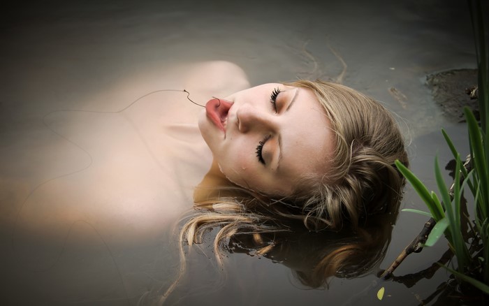 Woman with fishing line in mouth floating in water