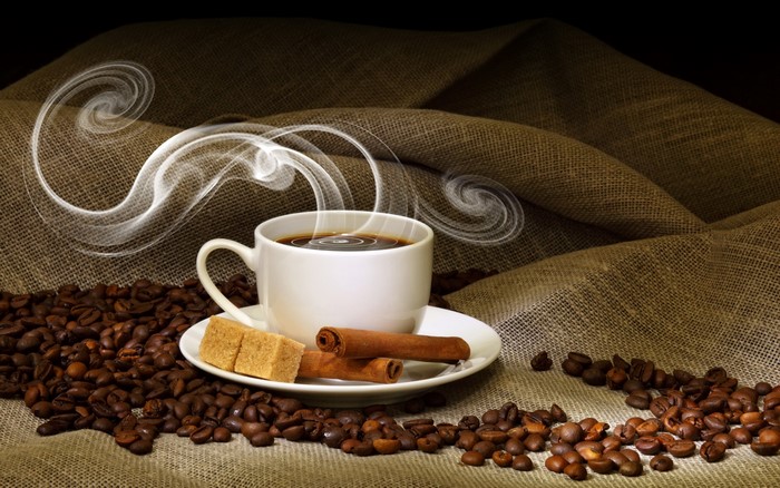 Steaming cup of coffee with cinnamon and sugar cubes