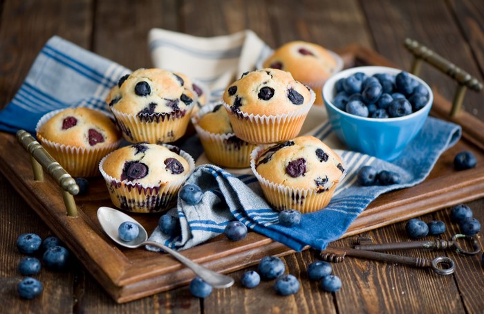 Blueberry muffins on a wooden tray with blueberries