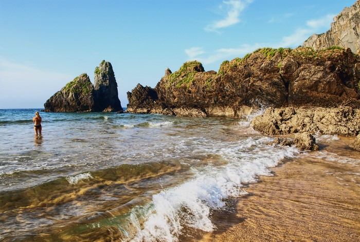 Woman in bikini standing in the sea near rocky coast
