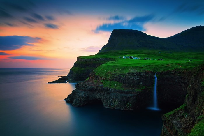 Waterfall cascading from a green cliff into the sea at sunset