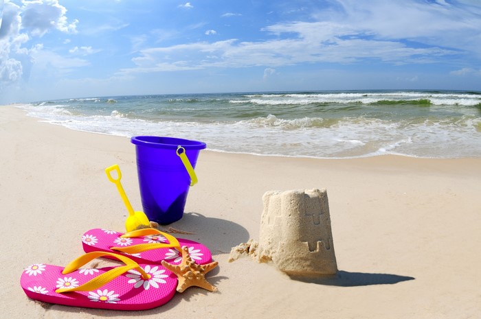 Beach scene with sandcastle, bucket, shovel, and flip-flops