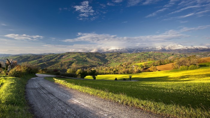 Winding road through rolling hills and snow-capped mountains
