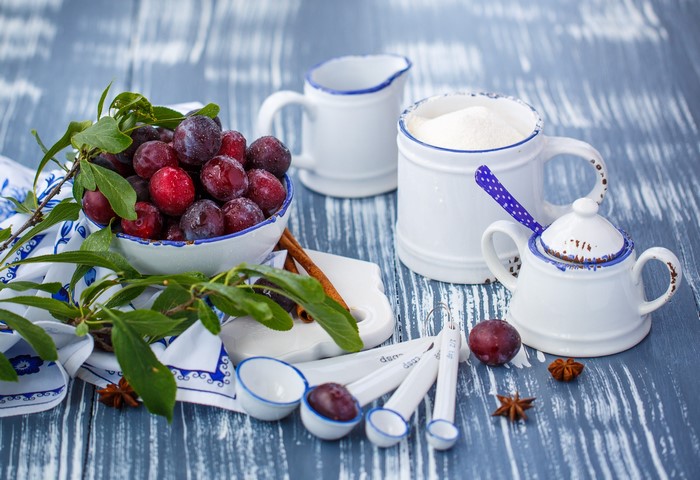 Plums in a bowl with measuring spoons and sugar