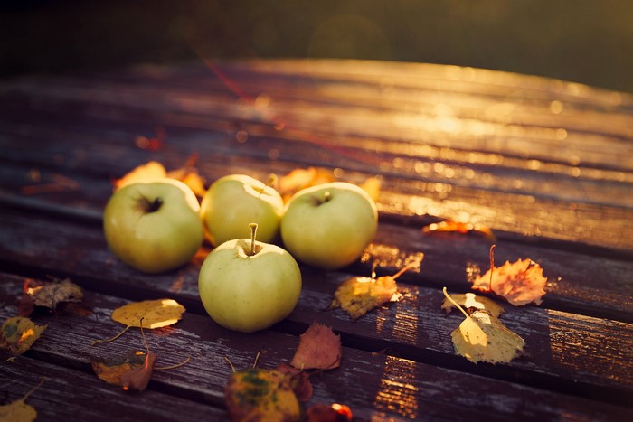 Apples on a wooden table with autumn leaves