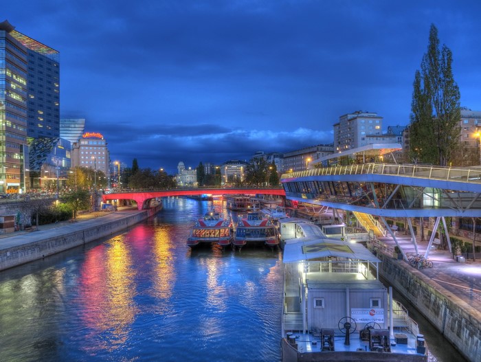 Riverboats on a canal at night with a red bridge