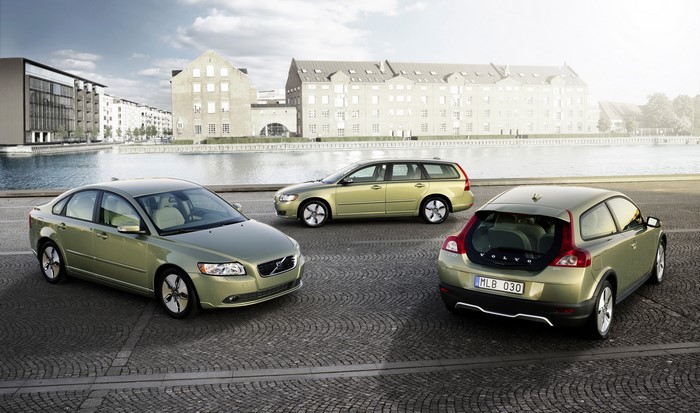 Three Volvo cars parked on cobblestone by a canal