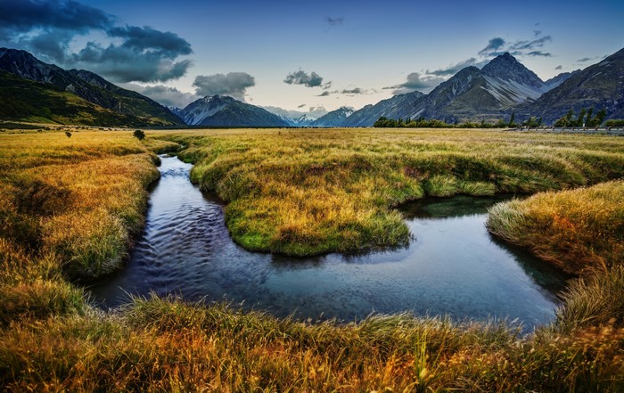 River flowing through a grassy plain with mountains in the background