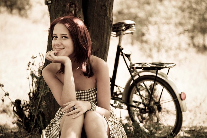 Redhead girl smiling sitting by a bicycle