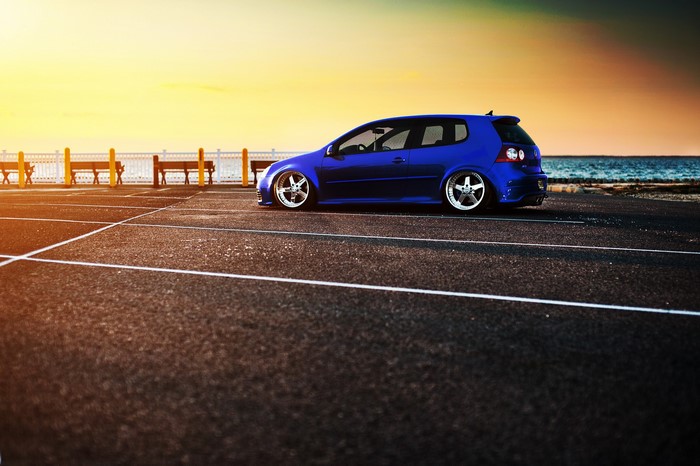 Blue Volkswagen Golf parked by the sea at sunset