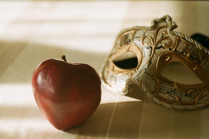 Red apple and a Venetian mask on a striped cloth
