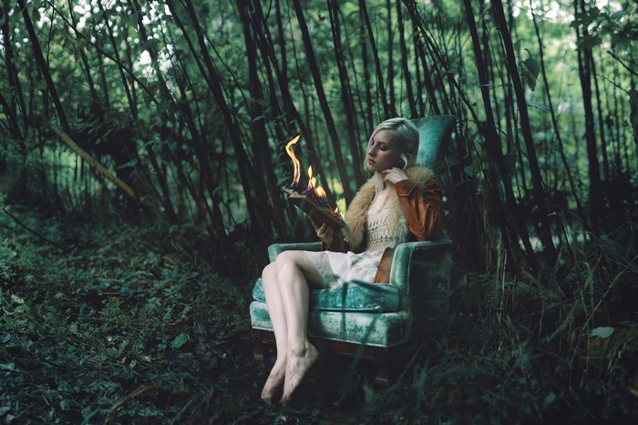 Woman reading a burning book in an armchair in the forest