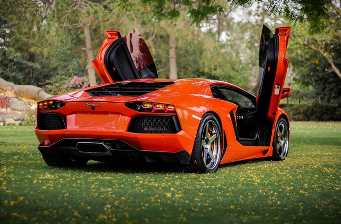 Orange Lamborghini Aventador LP700-4 with doors open on grass