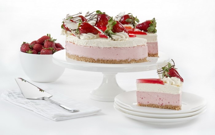 Strawberry cheesecake on a white cake stand with a slice on a plate
