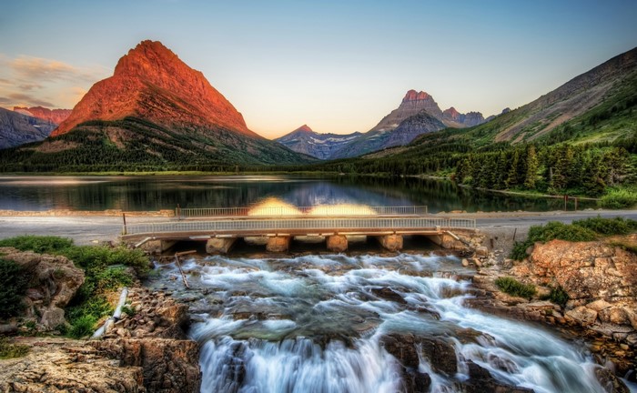 Sunrise over mountains and lake with bridge and waterfall