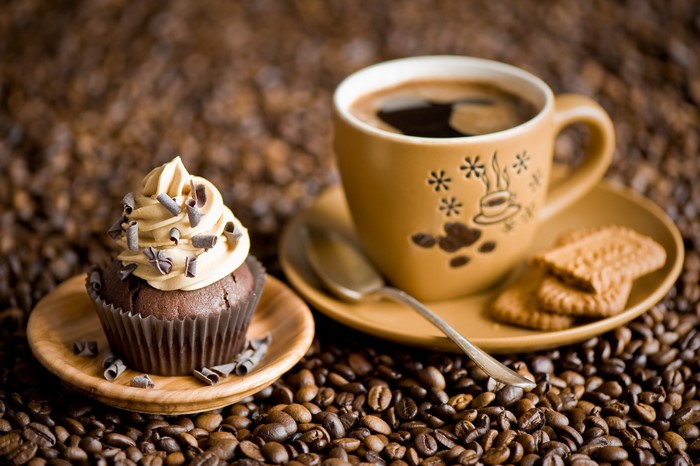 Cup of coffee with cupcake and cookies on coffee beans