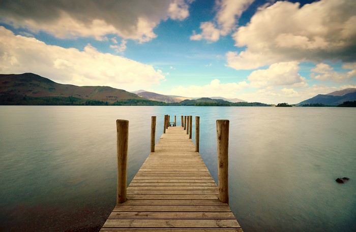 Wooden pier on a lake with mountains and clouds