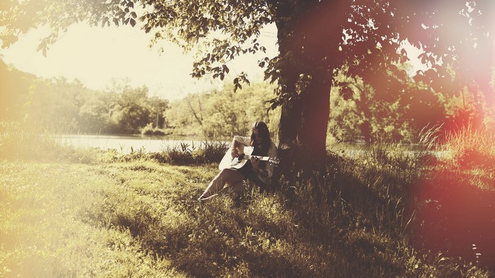 Woman playing guitar under a tree by a lake