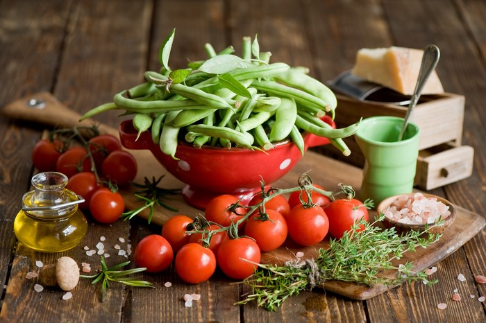 Green beans, tomatoes, olive oil, herbs, and cheese on a wooden table
