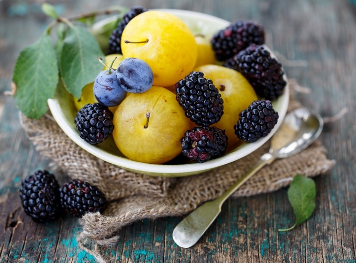 Bowl of yellow plums and blackberries with leaves
